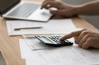 figure_photo: Person tippt auf Laptop und Taschenrechner